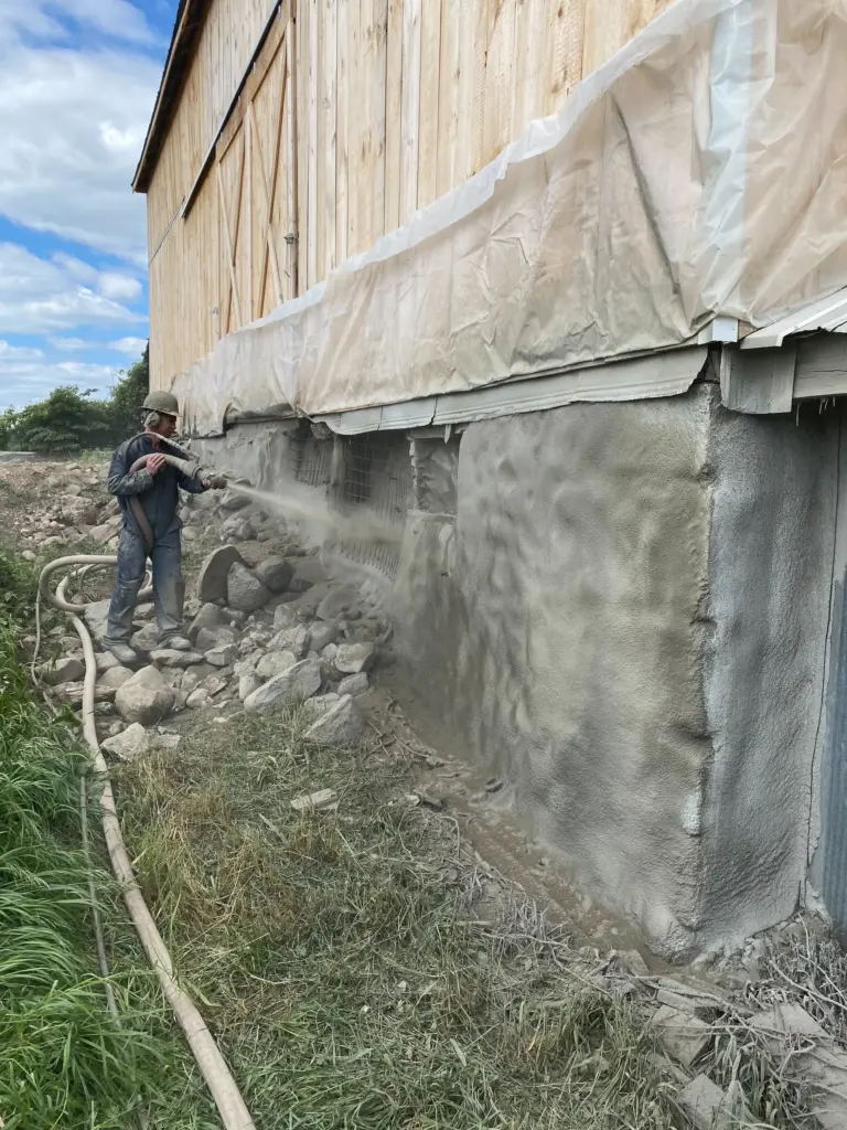 Professional structural foundation restoration for a timber frame barn using reinforced shotcrete (gunite) to stabilize and resurface a failing stone foundation.